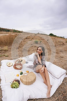 Beautiful woman with blond hair in elegant dress having picnic with mountains view