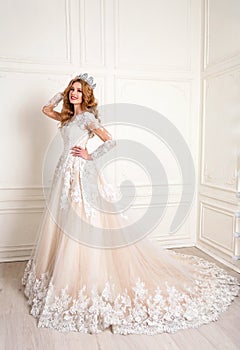 Beautiful woman with blond hair in luxurious wedding dress with elegant crown posing in studio