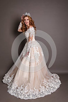 Beautiful woman with blond hair in luxurious wedding dress with elegant crown posing in studio