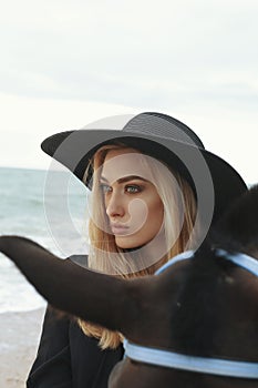 Beautiful woman with blond hair posing with black horse