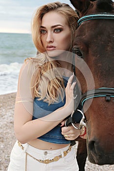 Beautiful woman with blond hair posing with black horse