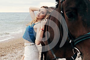 Beautiful woman with blond hair posing with black horse