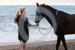 Beautiful woman with blond hair posing with black horse