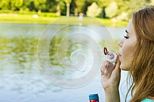 Beautiful woman blowing bubbles in the summer near the lake