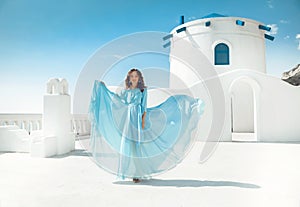 Beautiful woman in blowing chiffon dress posing by traditional greek white houses on Santorini, Greece. Attractive bride in