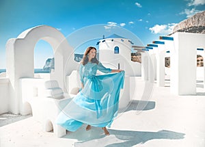 Beautiful woman in blowing chiffon dress posing by traditional greek white houses on Santorini, Greece. Attractive bride in