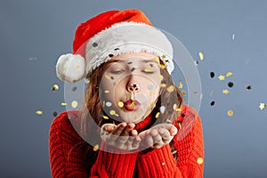 Beautiful woman is blowing confetti in the air, New Year party celebration. Isolated on gray background