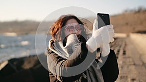 beautiful woman with blowing hair in pink sunglasses using smartphone and making selfie