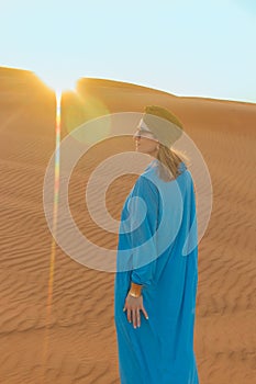 Beautiful woman in blue dress among the Dubai desert at sunset time