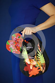 Beautiful woman in blue dress holding beach paraphernalia in her hands, like flip flops, sunglasses and beach bag