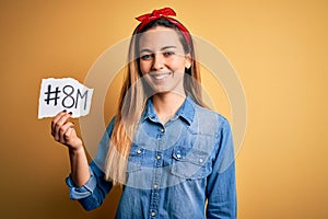 Beautiful woman with blue eyes celebrating 8th march womens day over yellow background with a happy face standing and smiling with