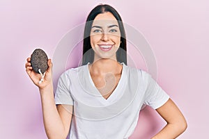 Beautiful woman with blue eyes holding pumice stone looking positive and happy standing and smiling with a confident smile showing