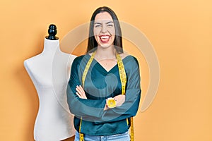 Beautiful woman with blue eyes standing by manikin with crossed arms sticking tongue out happy with funny expression