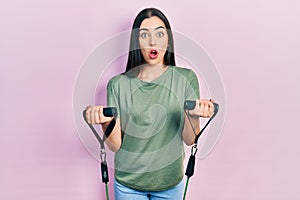 Beautiful woman with blue eyes training arm resistance with elastic arm bands afraid and shocked with surprise and amazed