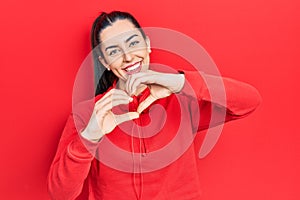Beautiful woman with blue eyes wearing gym clothes and headphones smiling in love showing heart symbol and shape with hands