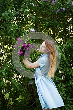 Beautiful woman in a blue summer dress with lilac flowers in a blooming garden. Spring Blossom