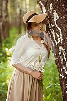 Beautiful woman with a bouquet of daisies near birch