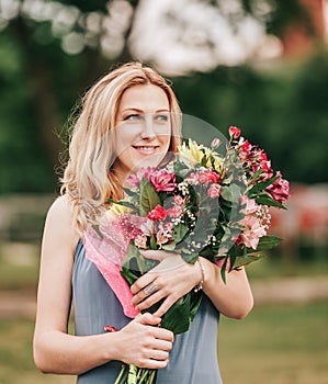 Beautiful woman with a bouquet of flowers standing on the grass in the city Park