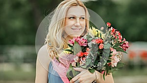 Beautiful woman with a bouquet of flowers standing on the grass in the city Park