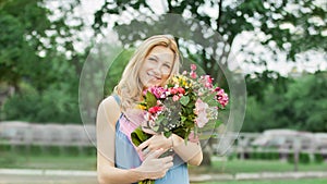 Beautiful woman with a bouquet of flowers standing on the grass in the city Park