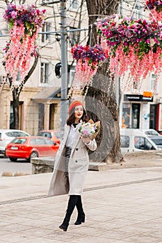 Beautiful woman with a bouquet of flowers walks along the city street