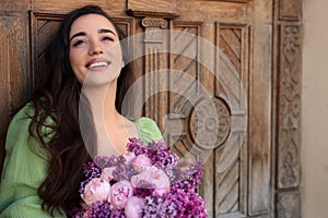 Beautiful woman with bouquet of spring flowers near wooden door, space for text