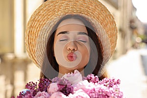 Beautiful woman with bouquet of spring flowers sending air kiss outdoors