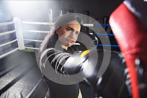 A beautiful woman in boxing gloves hits her paws in the ring. A young woman with a funny face hits the coach`s hand