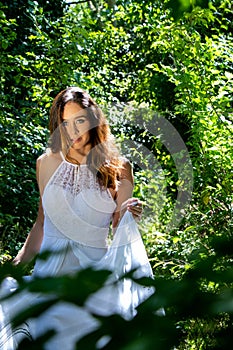 Beautiful woman, bride with blue eyes and brown hair walks through leafy woods, woodland on a bright sunny summer`s day