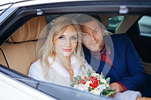 Beautiful woman bride with a bouquet of flowers and a man sitting in the car, looking out the window