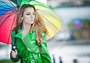 Beautiful woman in bright green coat posing in the rain holding a multicolored umbrella