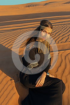 Beautiful woman in brilliant Burqa mask among the Dubai desert at sunset timeArabian style.