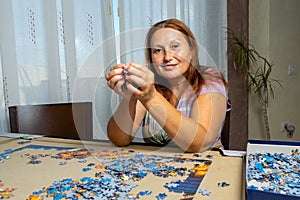 Beautiful woman with brown hair and in a colorful dress doing puzzle in the living room at home