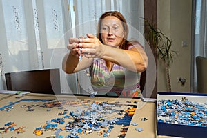 Beautiful woman with brown hair and in a colorful dress doing puzzle in the living room at home