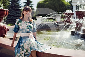 Beautiful woman-brunette in floral dress sitting near the founta