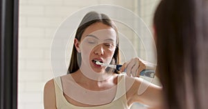 Beautiful woman brushing teeth looking in the mirror