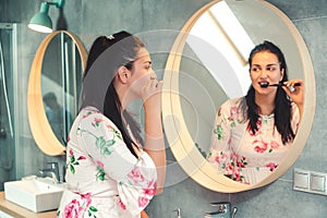 Beautiful woman brushing teeth in the morning. Girl looking in the mirror in the bathroom. Modern interior of bathroom. Teeth care