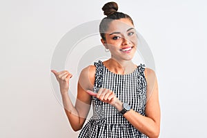 Beautiful woman with bun wearing casual dresss standing over isolated white background Pointing to the back behind with hand and