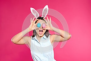 Beautiful woman in bunny ears headband holding Easter eggs near eyes