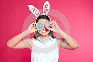 Beautiful woman in bunny ears headband holding Easter eggs near eyes