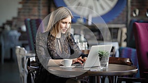 Beautiful woman in a cafe working with a laptop. A cheerful, happy girl, prints on the laptop`s keyboard, she received