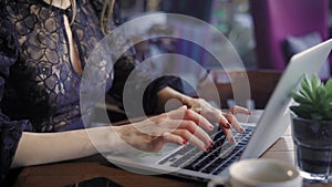 Beautiful woman in a cafe working with a laptop. A cheerful, happy girl, prints on the laptop`s keyboard, she received