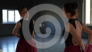 A beautiful woman came to the dance hall to warm up before training. The camera films the reflection in the wall mirror.