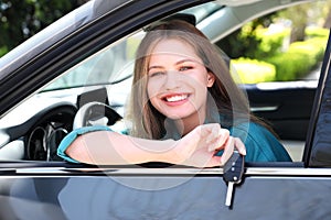 Beautiful woman with car key sitting in new auto