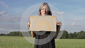 A beautiful woman with a cardboard poster stands in a field in the summer