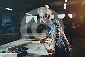 Beautiful woman carpenter designer works with ruler, make notches on the tree in workshop. Image of modern femininity. Concept o