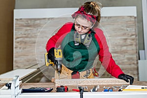 Beautiful woman carpenter drilling wooden plank, carpentry