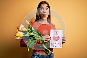 Beautiful woman celebrating mothers day holding love mom message and bouquet of tulips scared in shock with a surprise face,