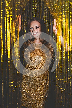 Beautiful woman celebrity with makeup wearing gold dress on golden bokeh background.