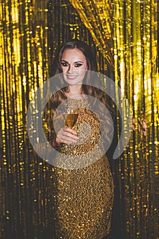 Beautiful woman celebrity with makeup wearing gold dress on golden bokeh background.